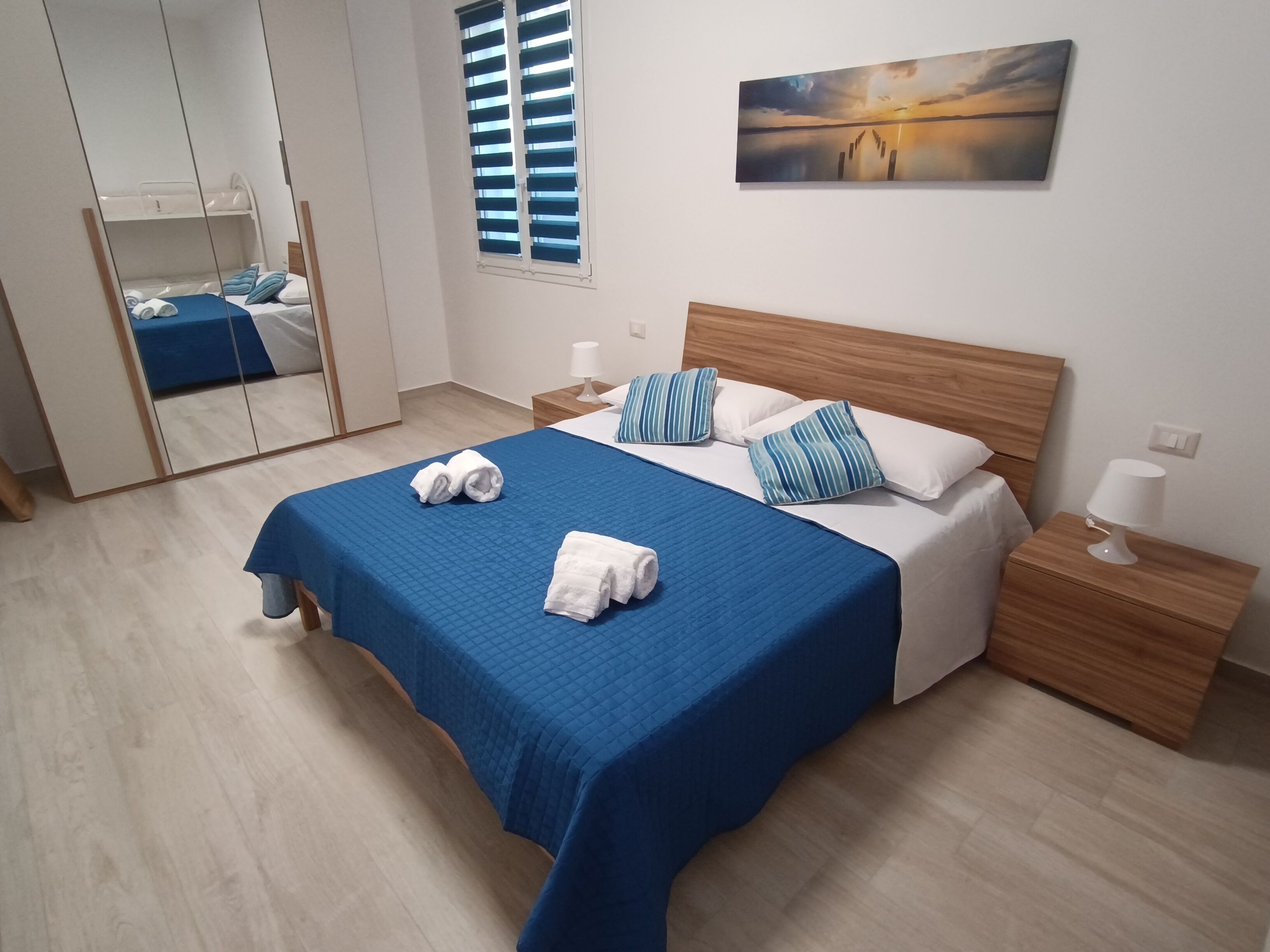 Un dormitorio con una cama, dos mesitas de noche, un espejo, una ventana y un cuadro en la pared.