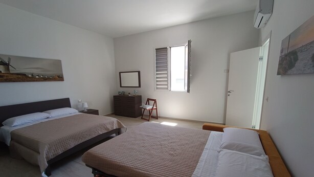 A hotel room with two beds, a dresser, a chair, a window with blinds, and a painting on the wall. - Vacation Home 300 m from the Sea, Ideal for Those Seeking Relaxation, Privacy, and Comfort (Avola)