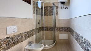 Casa de banho com chuveiro em cabine de vidro, duas sanitas, um bidé e um porta-toalhas.