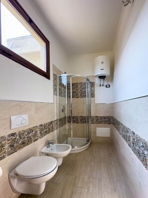 A bathroom with a glass-enclosed shower, two toilets, a bidet, and a towel rack. - Casa Helios Cozy Penthouse (Sassari)