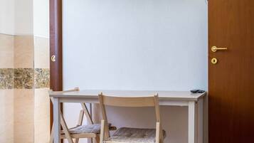 Una habitación con un escritorio de madera, dos sillas, un televisor montado en la pared y una puerta de madera.