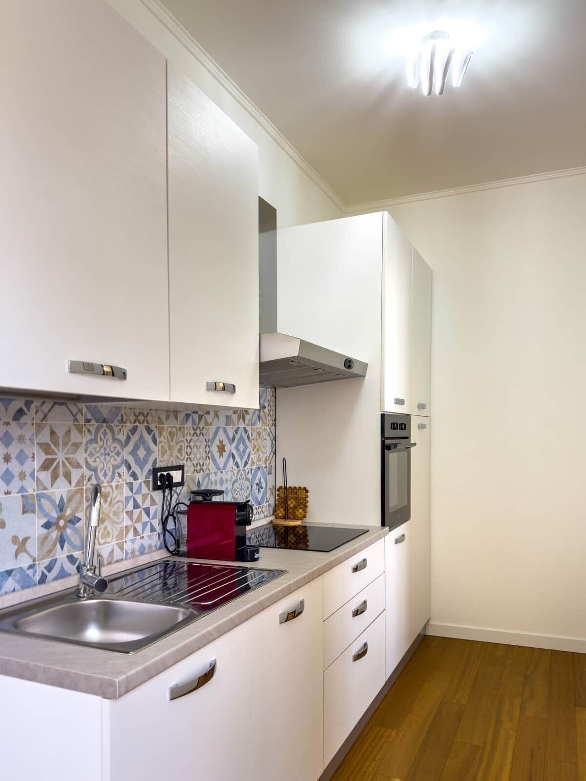 Cozinha moderna com armários brancos, pia de aço inoxidável e forno embutido.