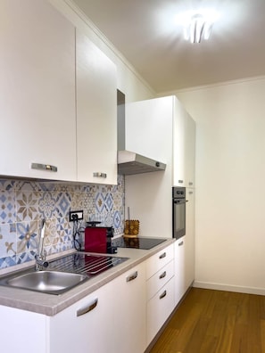Una cocina moderna con armarios blancos, un lavamanos de acero inoxidable y un horno empotrado.