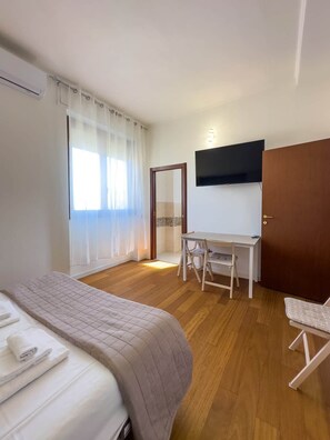A hotel room with a bed, a desk, a chair, a television, and a door. - Casa Helios Cozy Penthouse (Sassari)