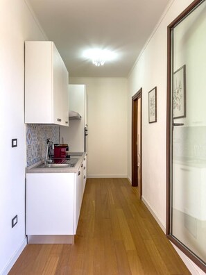 A narrow hallway with a kitchen area on the left, featuring white cabinets, a stove, and a tiled backsplash. - Casa Helios Cozy Penthouse (Sassari)