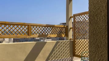 Un balcone con un recinto in legno a griglia, una sedia verde e un pavimento piastrellato.