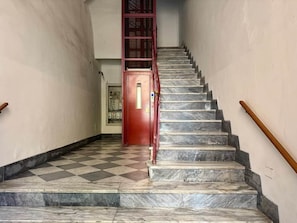Uma escadaria de mármore com corrimão vermelho que leva a uma porta.
