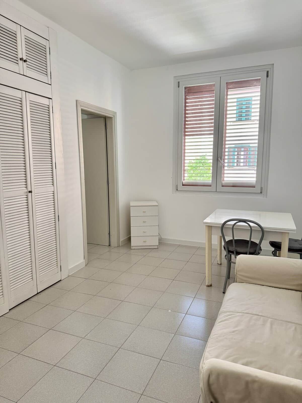 A room with a bed, a desk, a chair, a wardrobe, and a window with blinds.