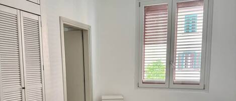 A room with a bed, a desk, a chair, a wardrobe, and a window with blinds.