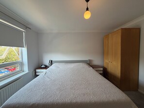 Une chambre à coucher avec un lit, une table de chevet, une armoire en bois et une fenêtre avec des stores.