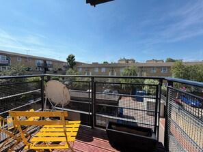 Un espace extérieur clôturé avec un banc jaune, une antenne parabolique et une poubelle.