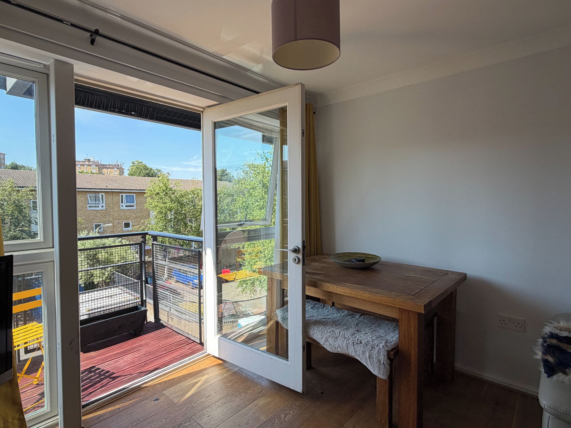 A room with a wooden table, a small rug, and a view of a balcony with a red mat.