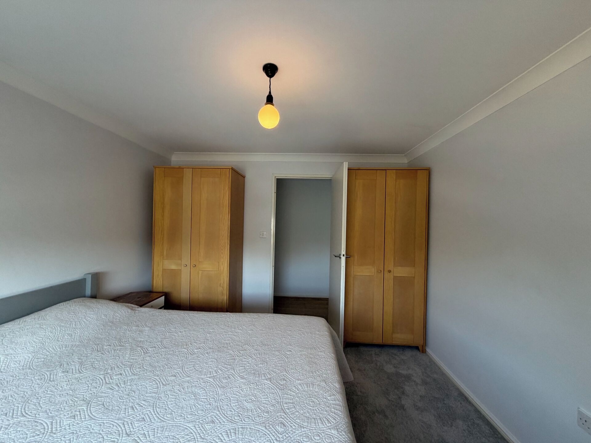 Ein Schlafzimmer mit einem Bett, zwei Holzschränken, einem Nachttisch und einer Hängelampe.