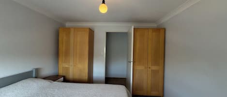 A bedroom with a bed, two wooden wardrobes, a nightstand, and a hanging light fixture.