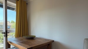 Ein Zimmer mit Holztisch, einer Schüssel, einem gelben Vorhang und Blick auf Gebäude.