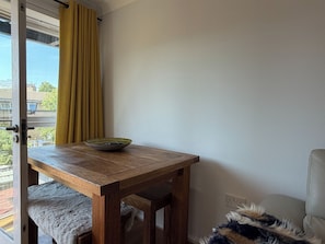 Ein Zimmer mit Holztisch, einer Schüssel, einem gelben Vorhang und Blick auf Gebäude.