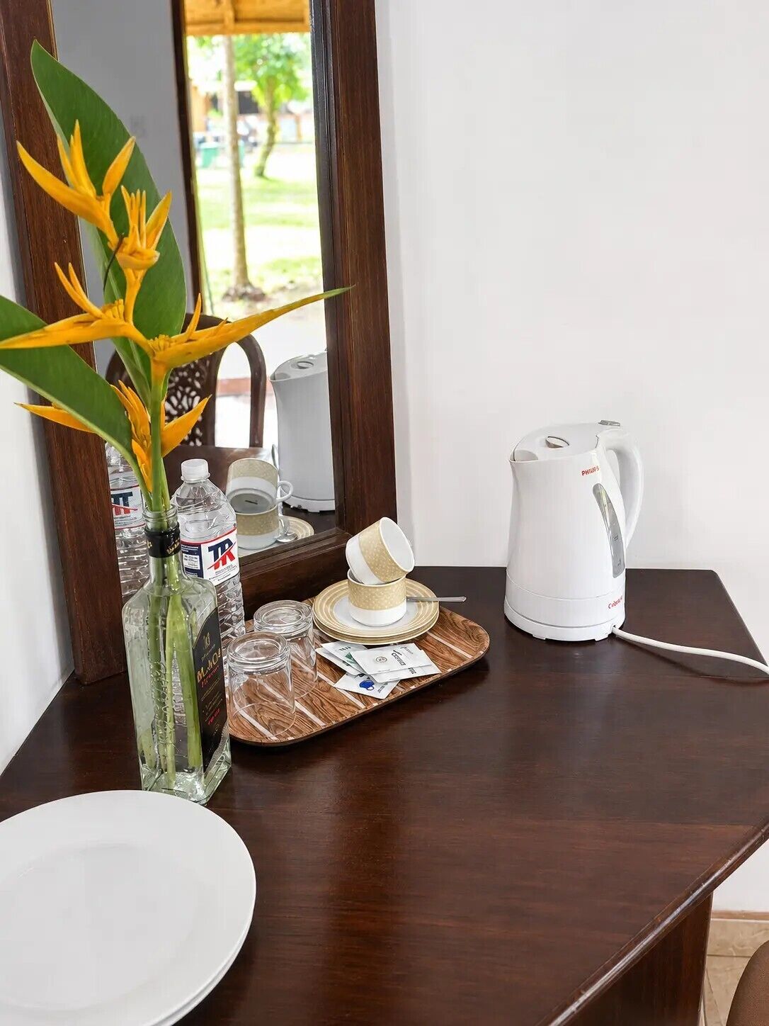 A wooden table with a white plate, a glass bottle, a white kettle, and a tray with a cup and saucer.