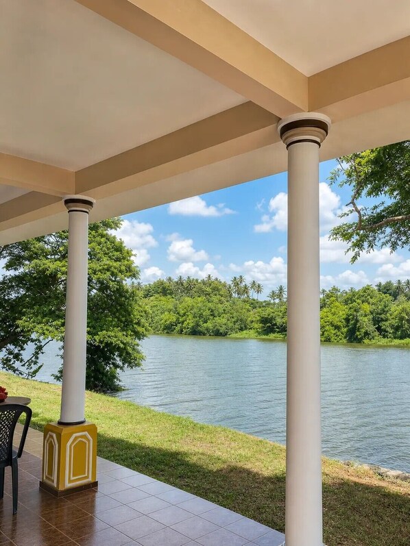 A covered outdoor area with columns, a view of a lake, and a grassy area.