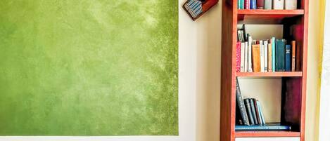 Un dormitorio con cama, mesita de noche, estantería y pared verde.
