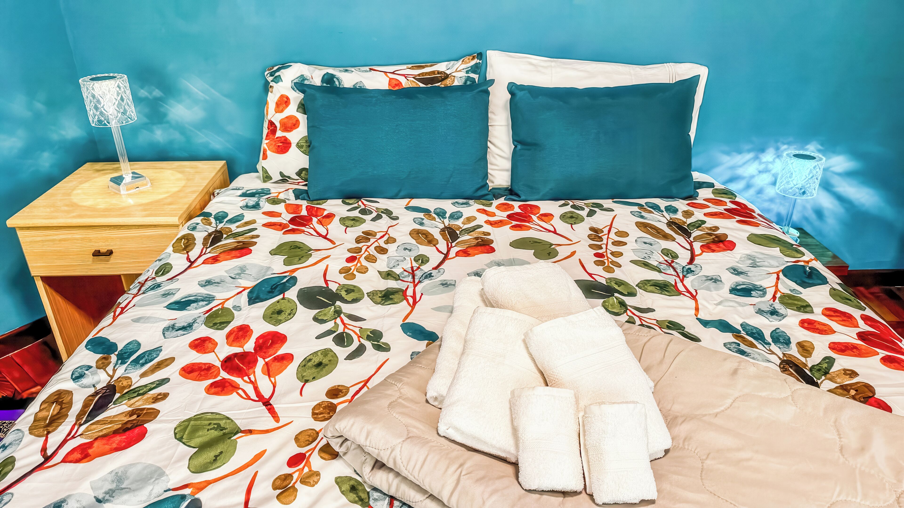 A bed with floral bedding, a wooden nightstand, and a lamp.