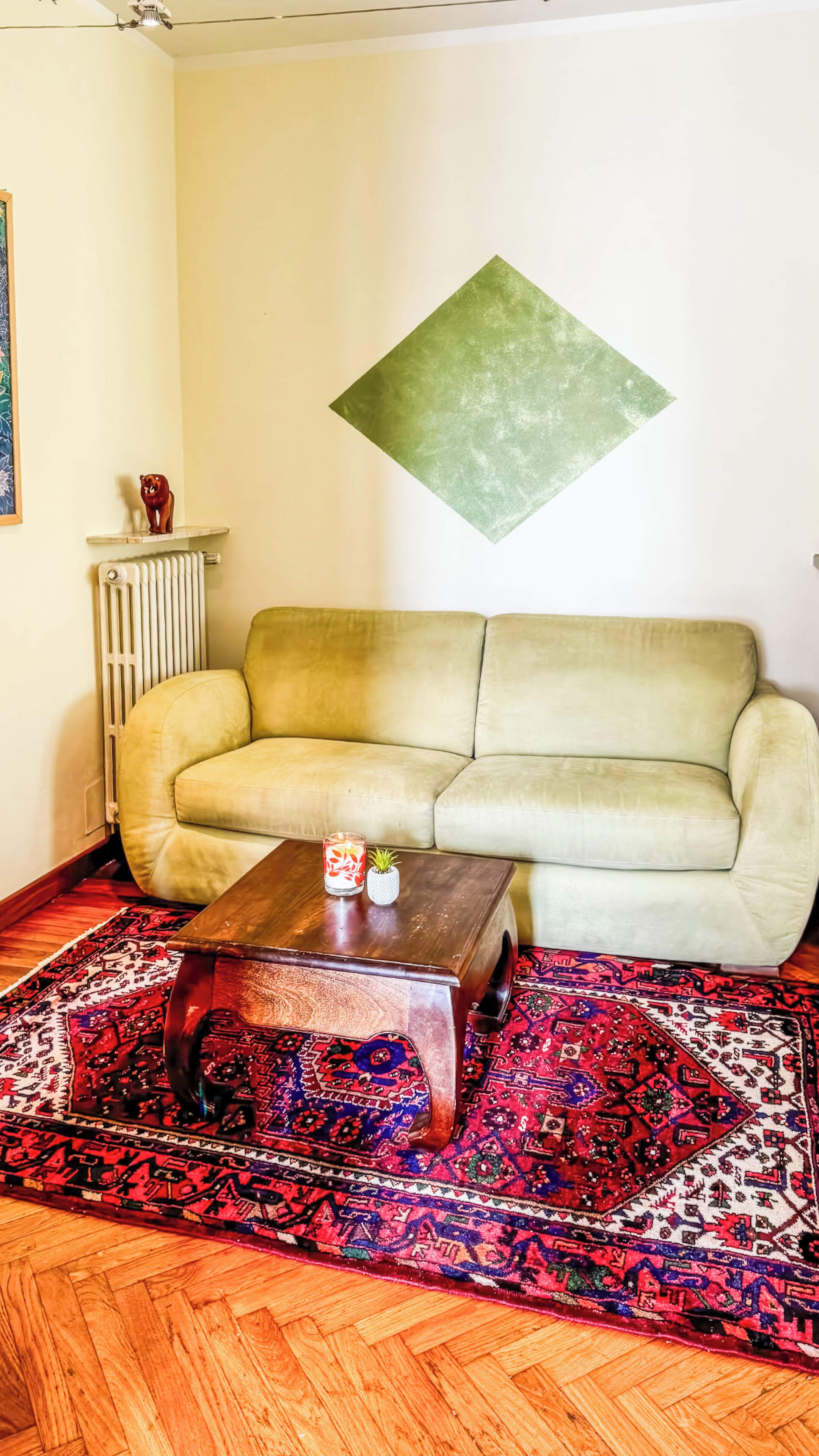 Un salon comprenant un canapé, une table basse, un radiateur, un tapis décoratif et une œuvre d’art en forme de losange accrochée au mur.