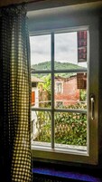 Una ventana con marco de metal, vista de un edificio de ladrillo y una colina verde al fondo.