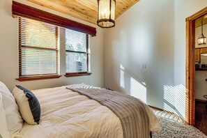 A bedroom with a bed, a window with blinds, a wooden ceiling, and a door leading to a kitchen. - Torreon Family Retreat, 4BR Mountain Home (Show Low)