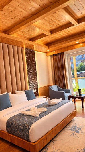 A hotel room with a large bed, a seating area with a chair, and a view of the outdoors through a window. - Hotel Rudra Grand (Manali)