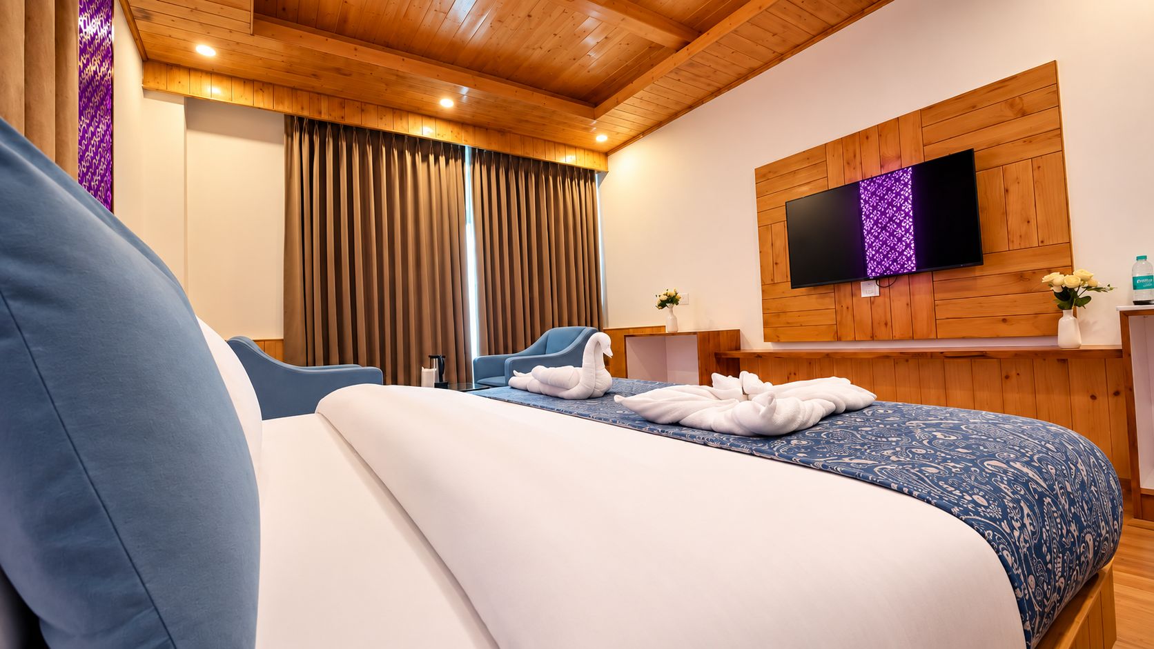 Une chambre d’hôtel avec un lit, deux chaises, un téléviseur et un lambris en bois.