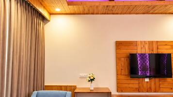 A room with a wooden ceiling, a blue sofa, a wooden table with a kettle, a TV on a wooden wall, and a patterned rug.
