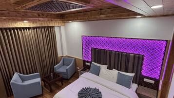 Une chambre moderne avec un plafond en bois, un grand lit avec une literie blanche, deux fauteuils et un luminaire fixé au mur.
