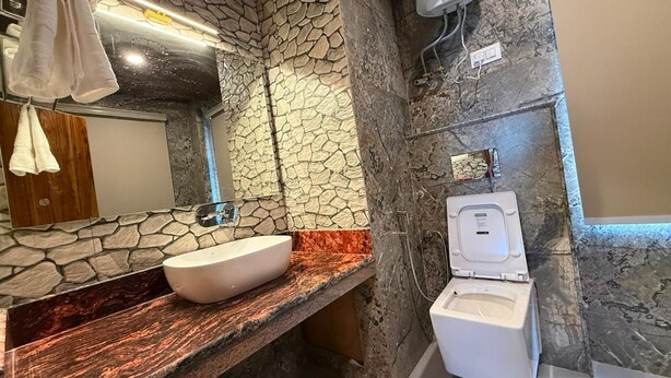 Un baño con pared de piedra, encimera de mármol, lavabo blanco e inodoro.