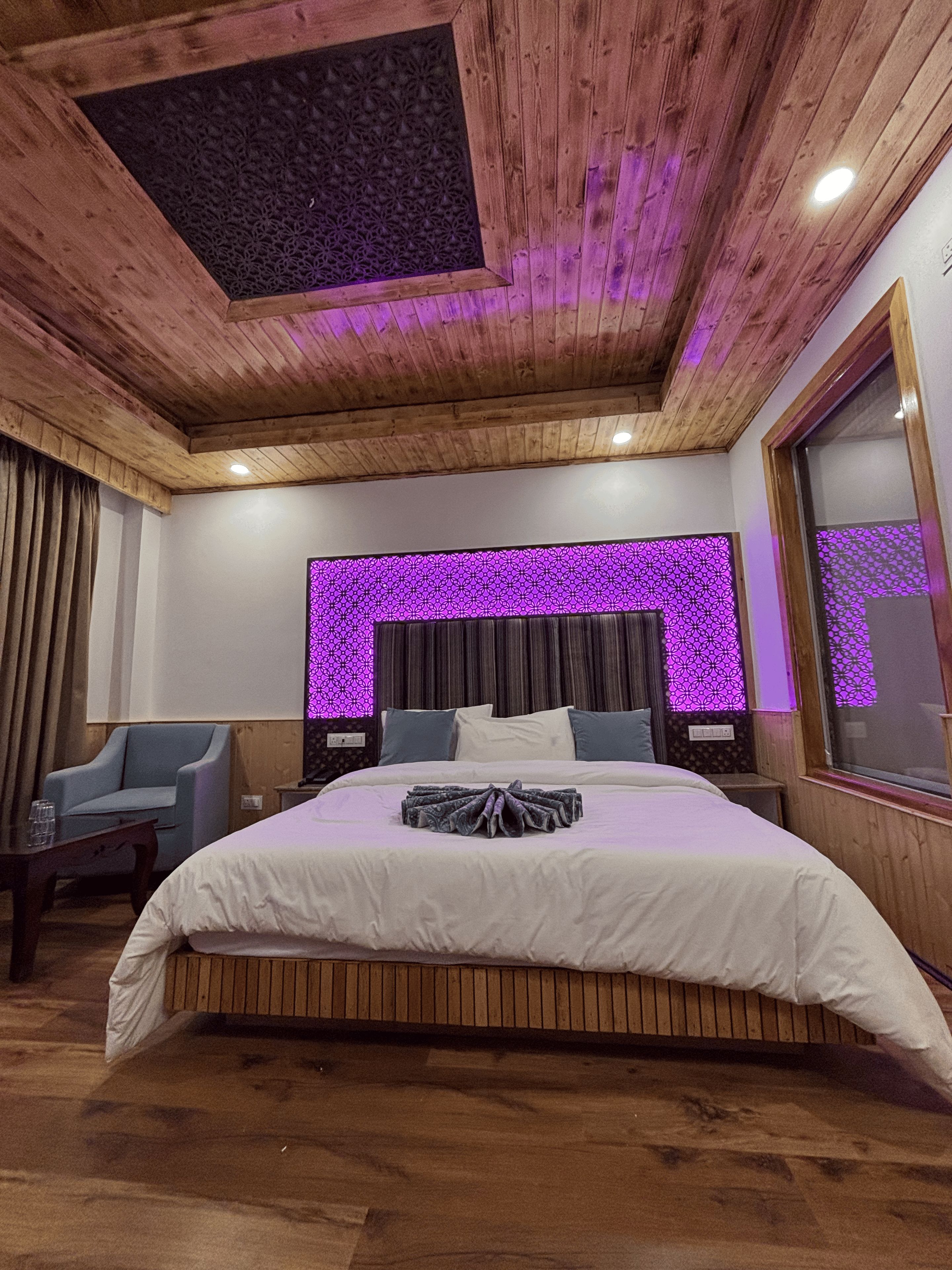Une chambre à coucher avec un plafond en bois, un grand lit, une table de chevet, une chaise et une fenêtre avec des rideaux.