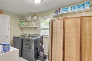 A laundry area with two washing machines, a dryer, and a vacuum cleaner. There are shelves with toiletries and paper products. - 4 Mi to Dtwn! 'Carolyn's Cottage' in Decatur (Decatur)