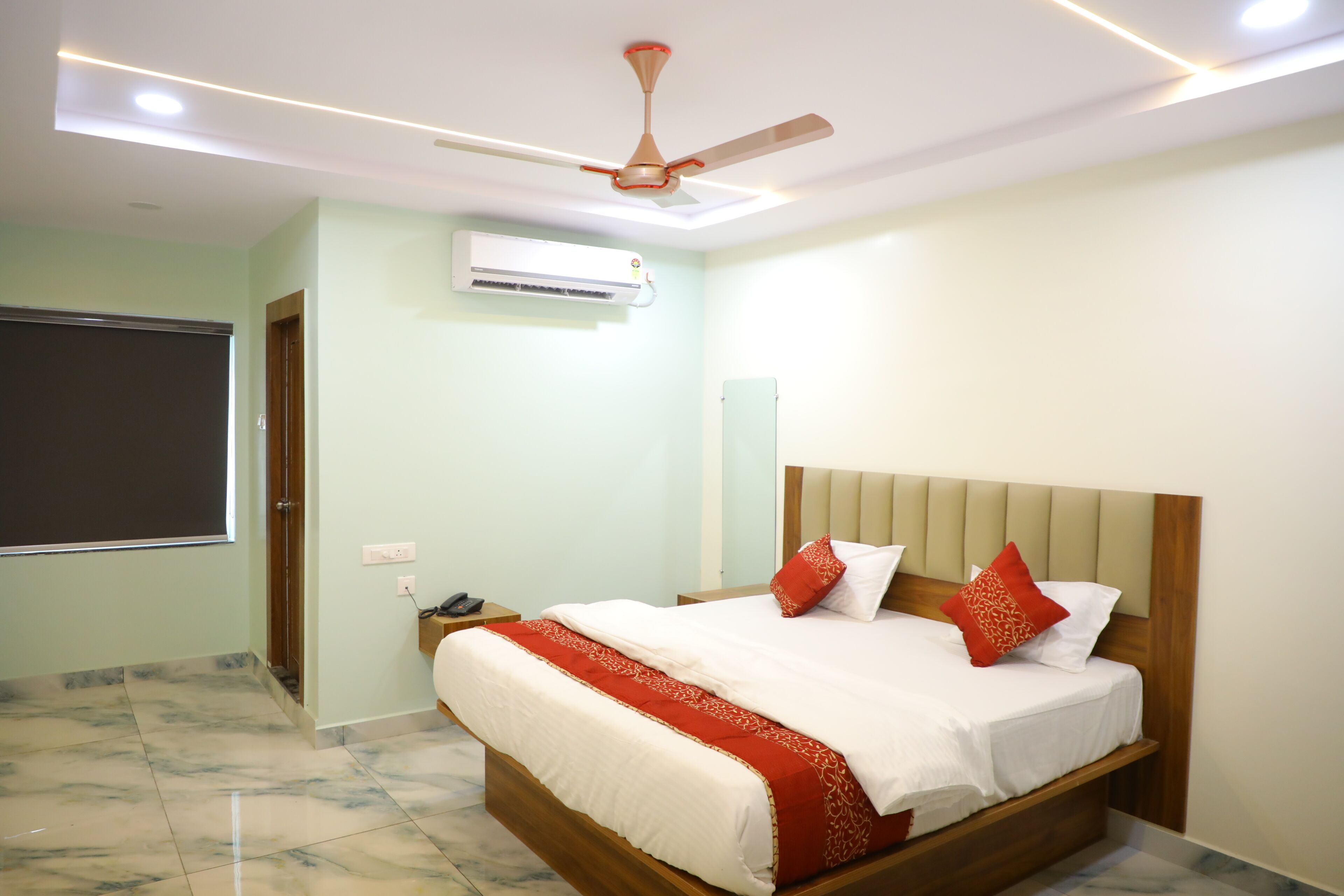 A bedroom with a bed, a ceiling fan, an air conditioning unit, and a window.