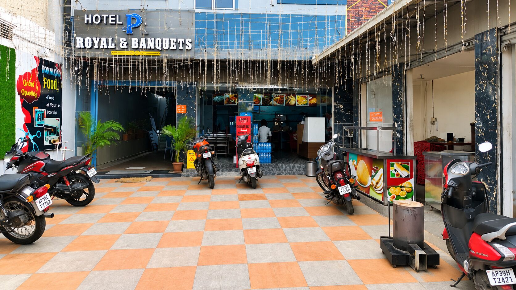 A hotel entrance with a checkered floor, motorcycles parked outside, and a sign for 'ROYAL & BANQUETS'.