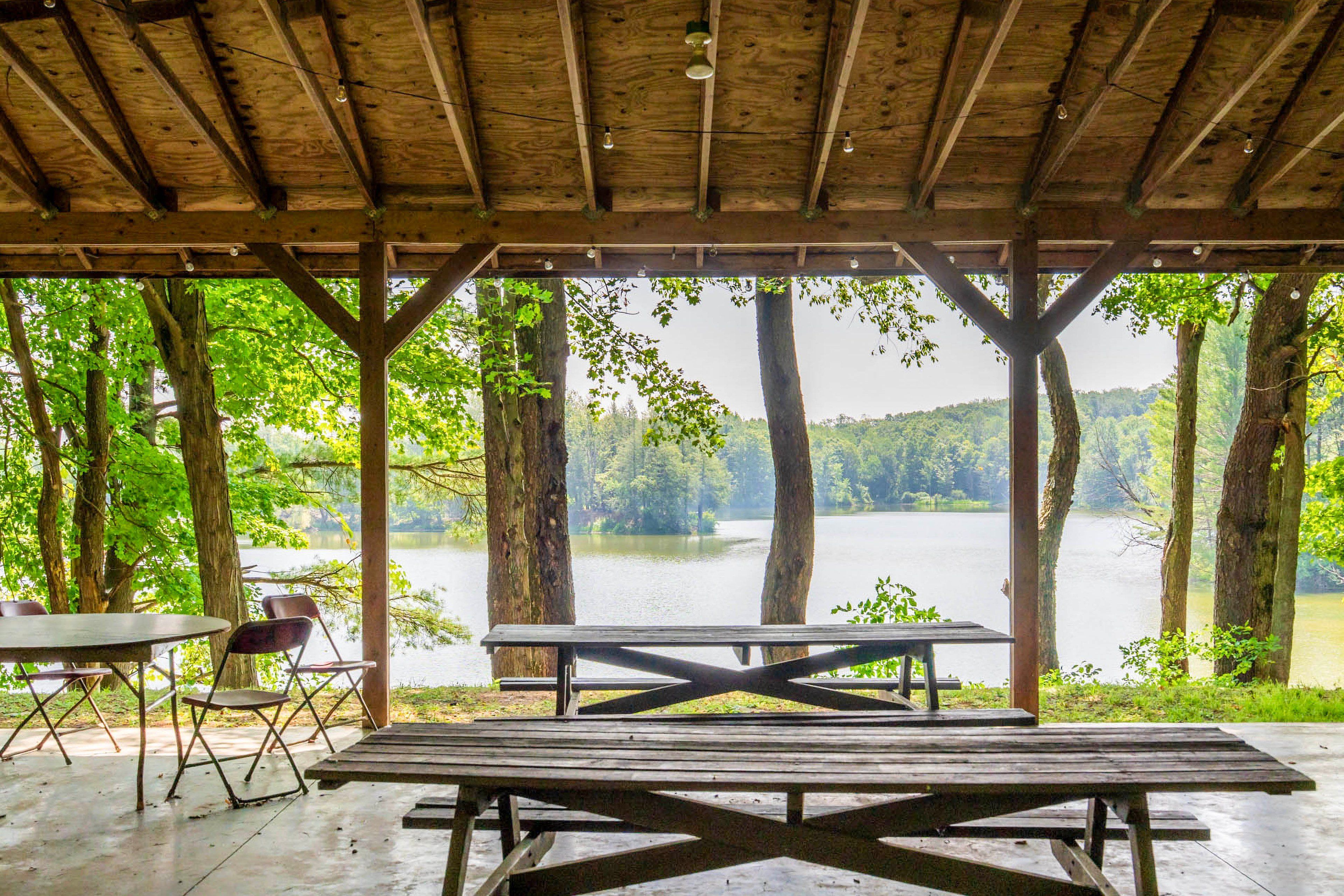 A covered picnic area with a view of a lake surrounded by trees.