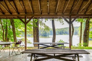 Un área de picnic techada con vista a un lago rodeado de árboles.