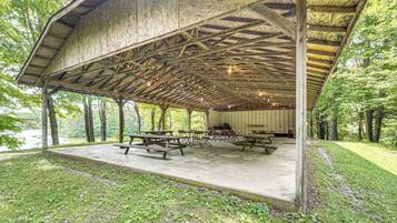 A covered picnic area with picnic tables and chairs, surrounded by trees and a body of water.