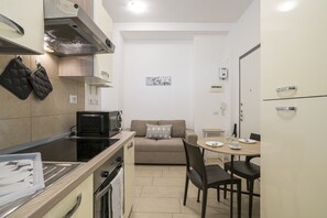 Eine kompakte Küche mit Mikrowelle, Herd und Backofen, ein beiges Sofa und ein Esstisch mit Stühlen.