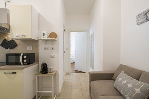 Ein kompakter Wohnbereich mit einer Küchenzeile, einem Sofa und einer Tür zu einem weiteren Raum.