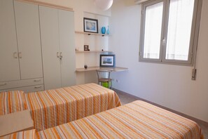 A room with two beds, a wardrobe, a shelf with pictures and vases, and a window. - Cozy apartment of about 90 sqm, able to accommodate up to 4 guests, located on the first floor of a modern building with an elevator. The property is situated in a residential area of ​​Pozzallo—a seaside town whose beaches have repeatedly been awa (Pozzallo)