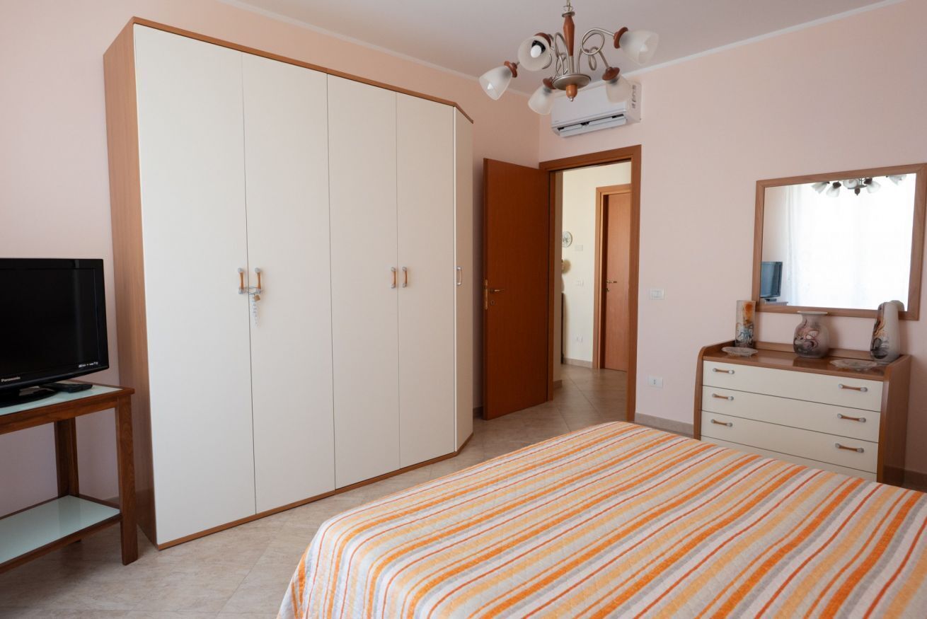 Ein Schlafzimmer mit Bett, Kleiderschrank, Fernseher, Kommode und Spiegel.