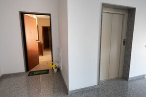 A hallway with a welcome mat, a door, and a potted plant. - Cozy apartment of about 90 sqm, able to accommodate up to 4 guests, located on the first floor of a modern building with an elevator. The property is situated in a residential area of ​​Pozzallo—a seaside town whose beaches have repeatedly been awa (Pozzallo)