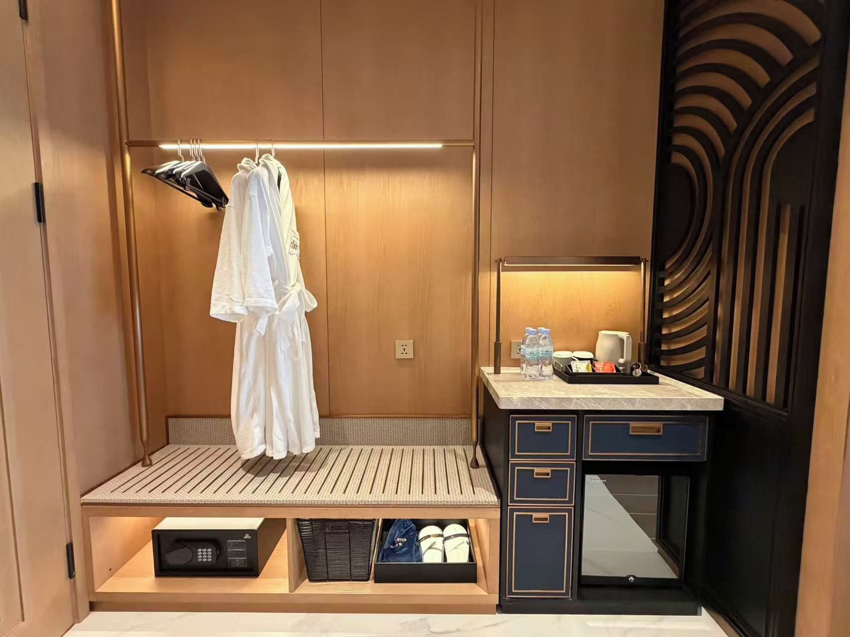 Une chambre d’hôtel avec une coiffeuse en bois, un miroir, un porte-serviettes et un petit coin salon équipé d’une table d’appoint.