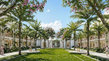 Un patio con palmeras, un sendero central y un edificio con balcones.