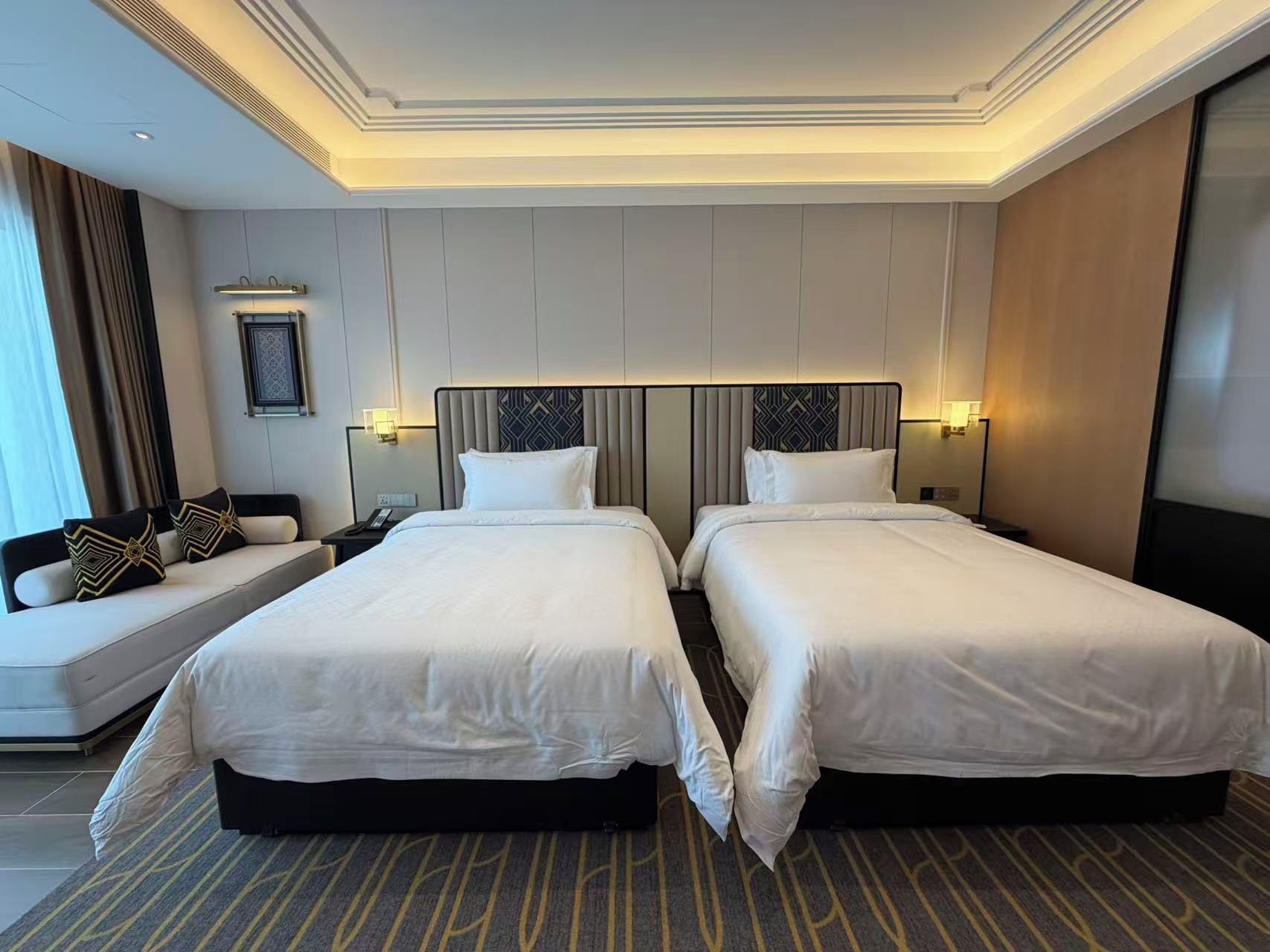 Habitación de hotel con dos camas, un sofá, una mesita de noche y una lámpara de pared.