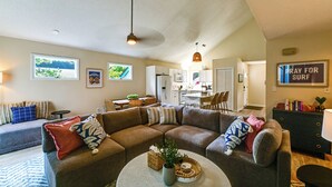 Uma sala de estar com sofá seccional, área de refeições e cozinha ao fundo.