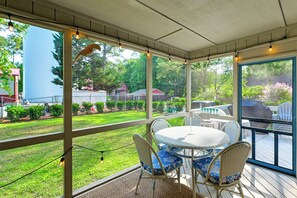 Une terrasse couverte avec une table et des chaises, donnant sur le jardin, et décorée de guirlandes lumineuses.