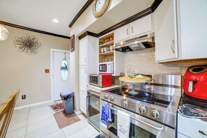 Eine Küche mit einem Edelstahlkochfeld, Backofen und einer Mikrowelle. Über der Arbeitsplatte befinden sich Schränke und an der Wand hängt eine Uhr.